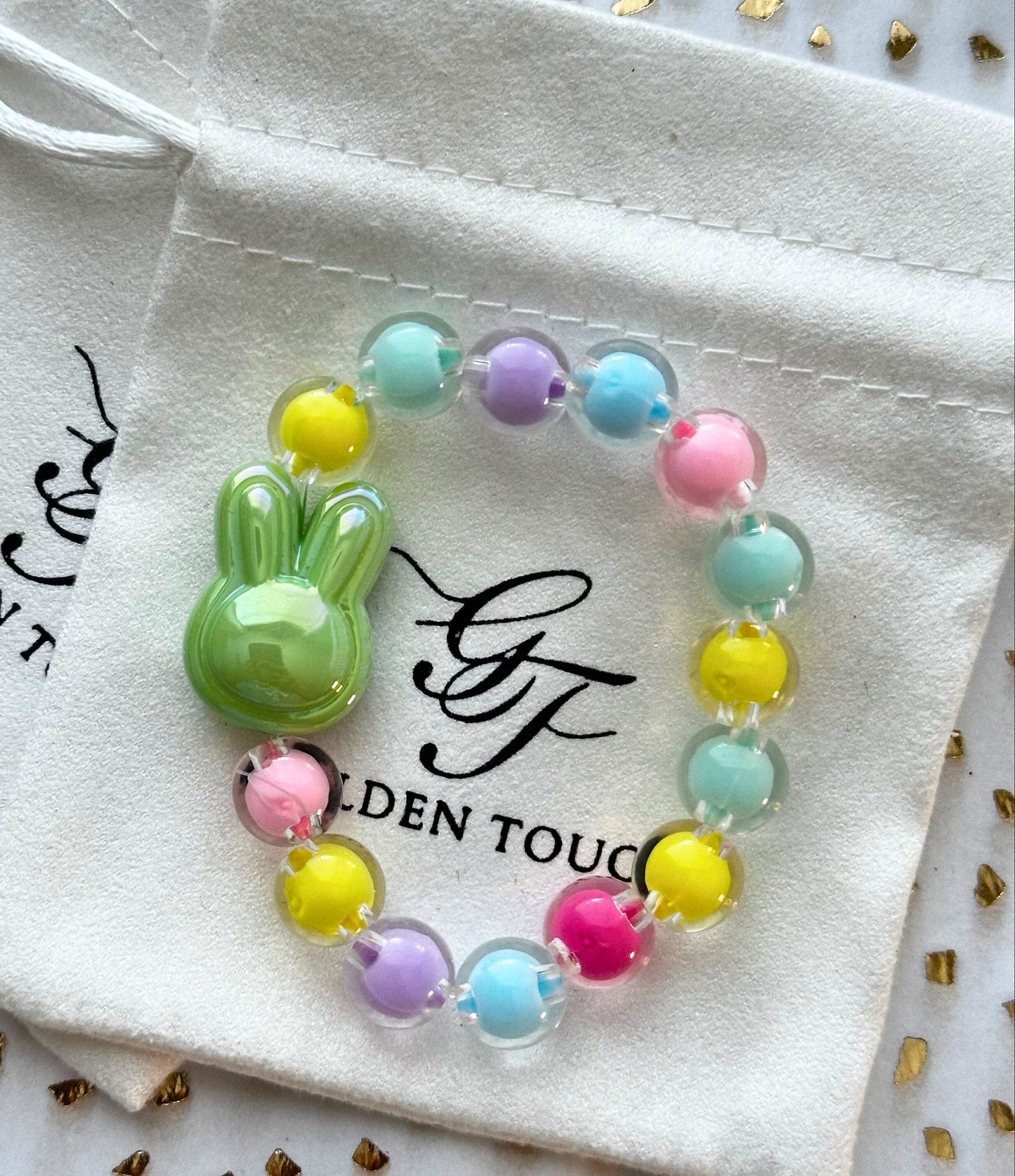 Colorful beaded bracelet with a green bunny charm on a Golden Touch branded pouch.