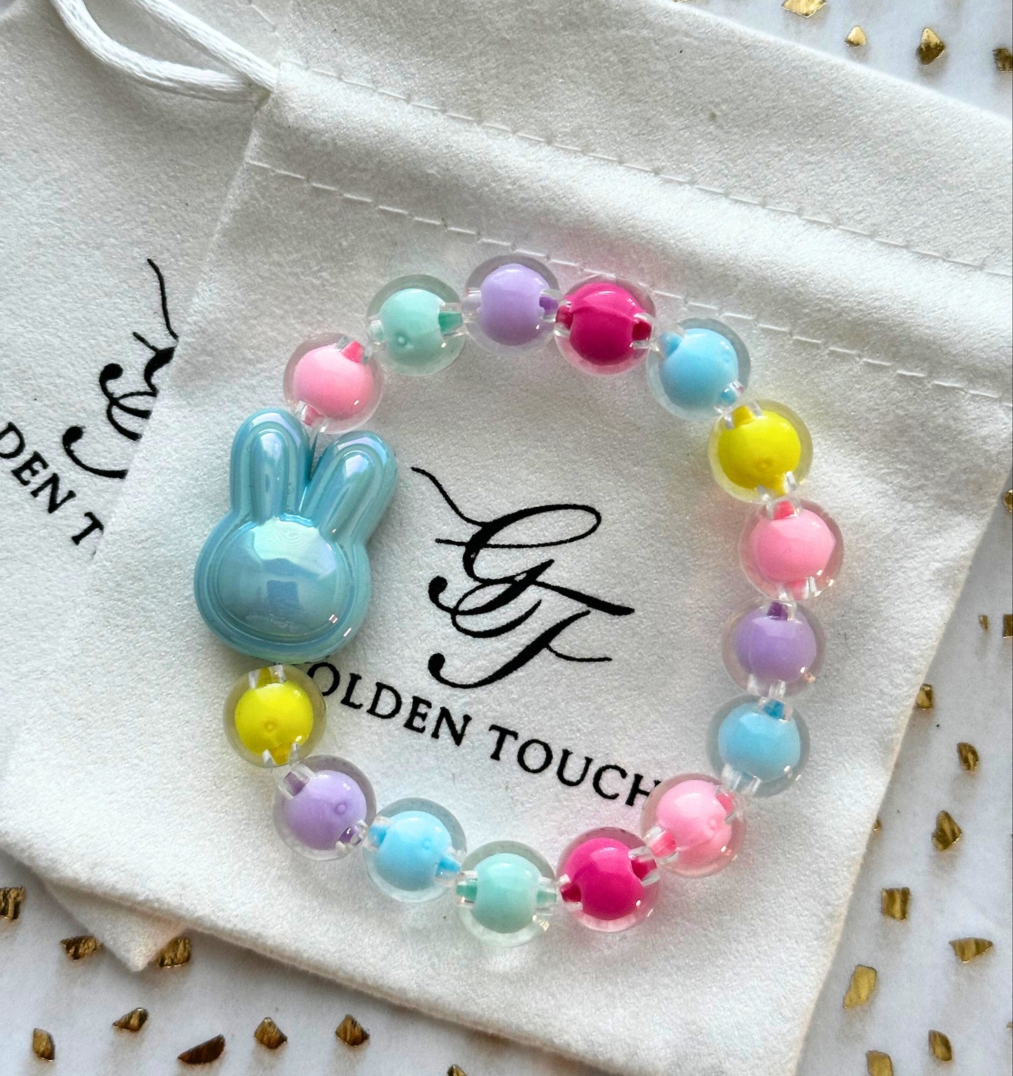 Colorful beaded bracelet with a bunny charm on a Golden Touch branded pouch.
