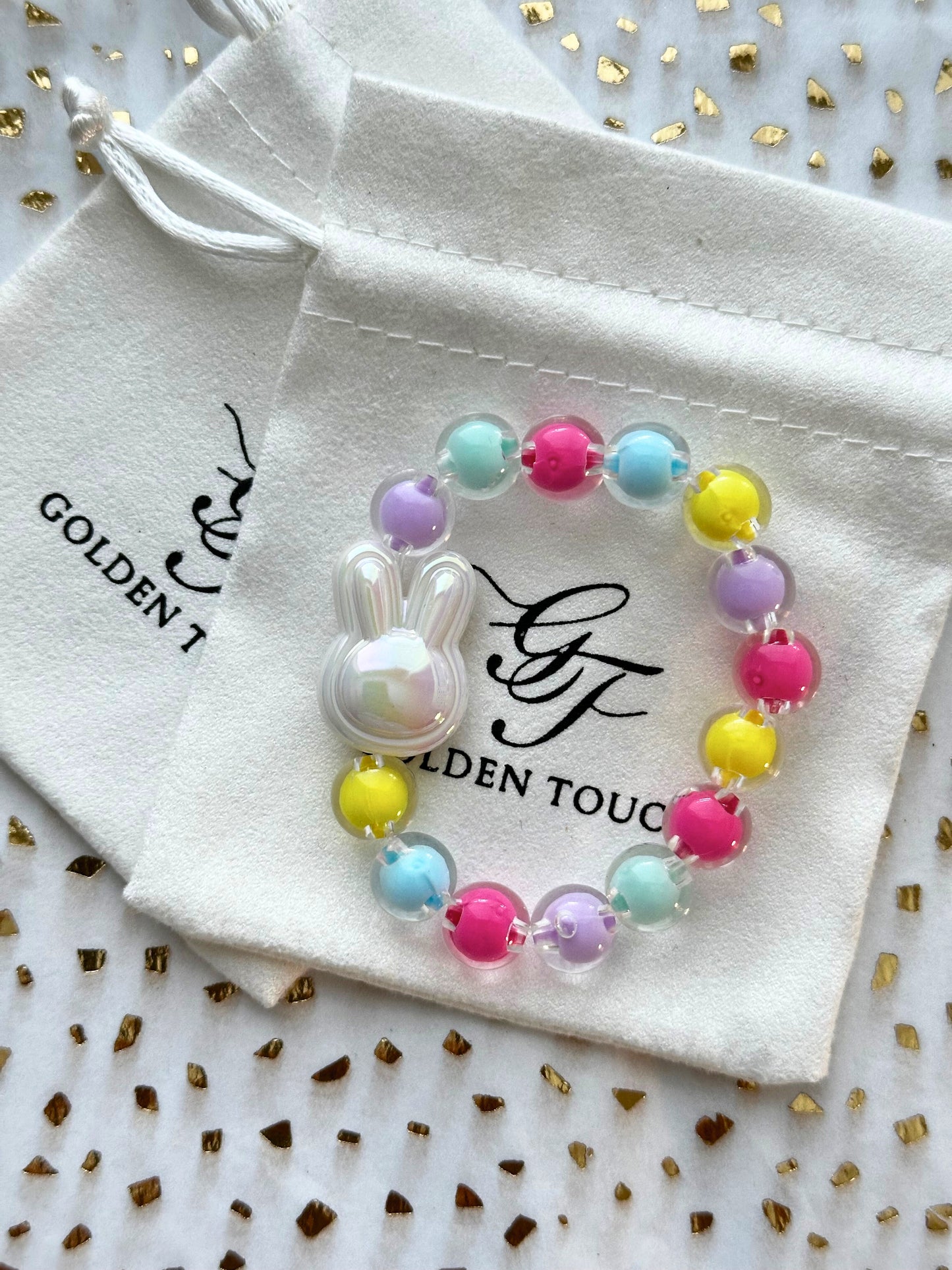 Colorful beaded bracelet with a bunny charm on a Golden Touch branded drawstring bag.