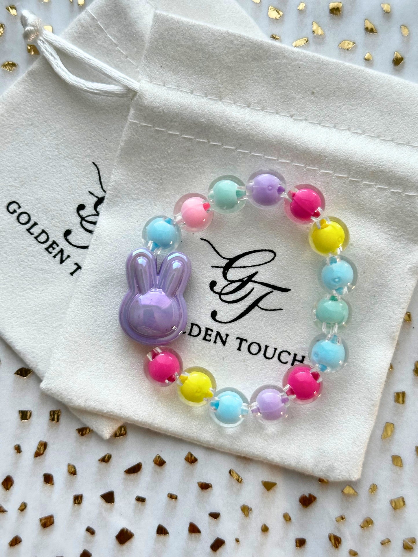 Colorful beaded bracelet with a bunny charm on a Golden Touch branded drawstring bag.