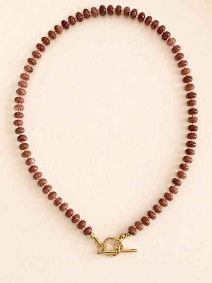 A beaded necklace made of small brown stone beads with a gold toggle clasp, displayed on a light beige background.