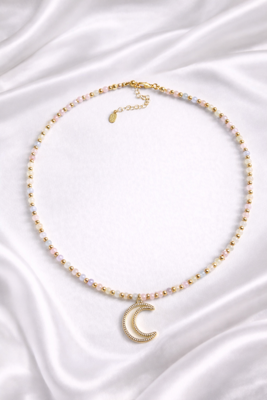 Necklace with light tone agate beads a gold crescent moon pendant on a white satin background