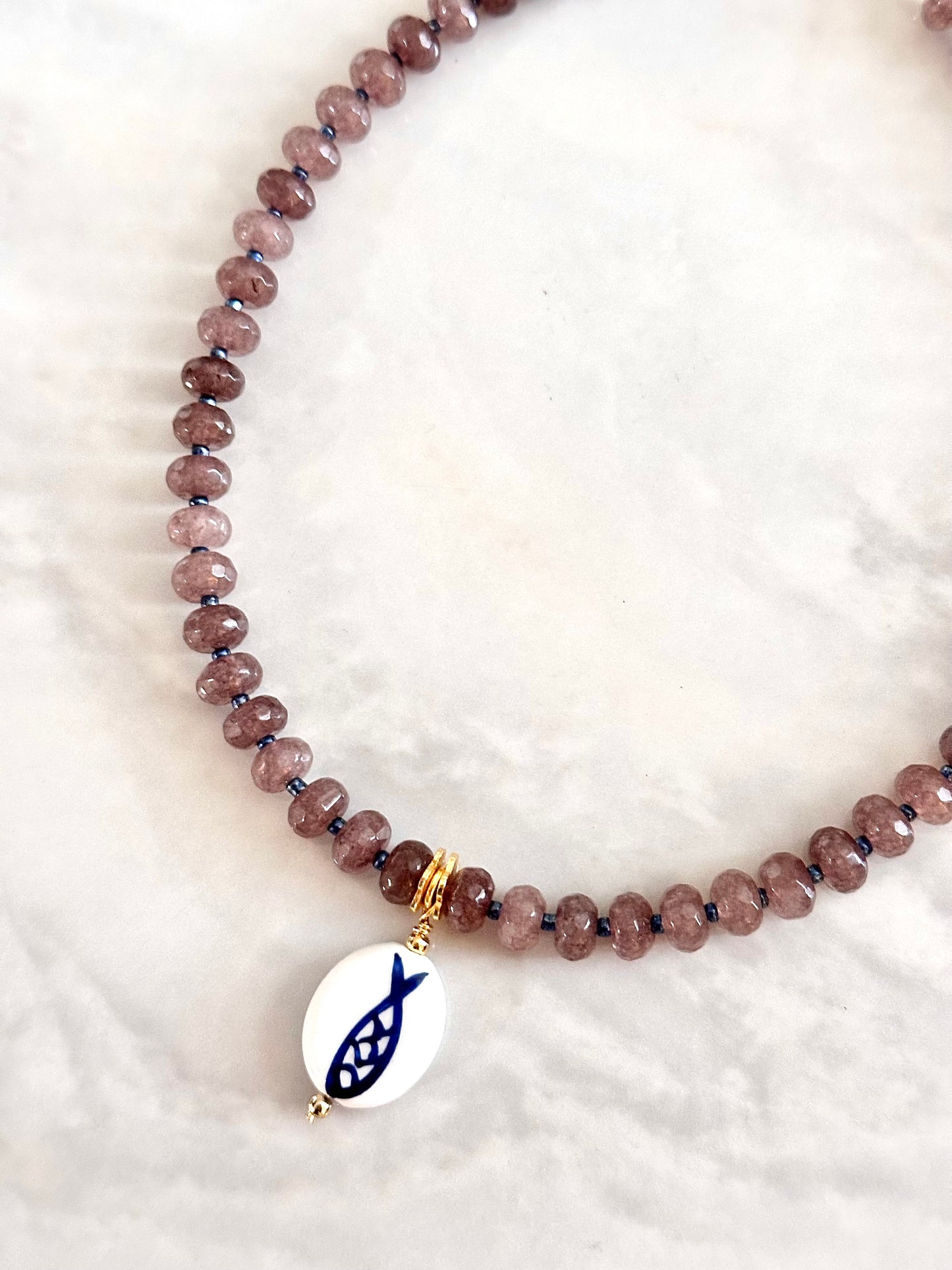 Beaded necklace with a fish charm on a white background