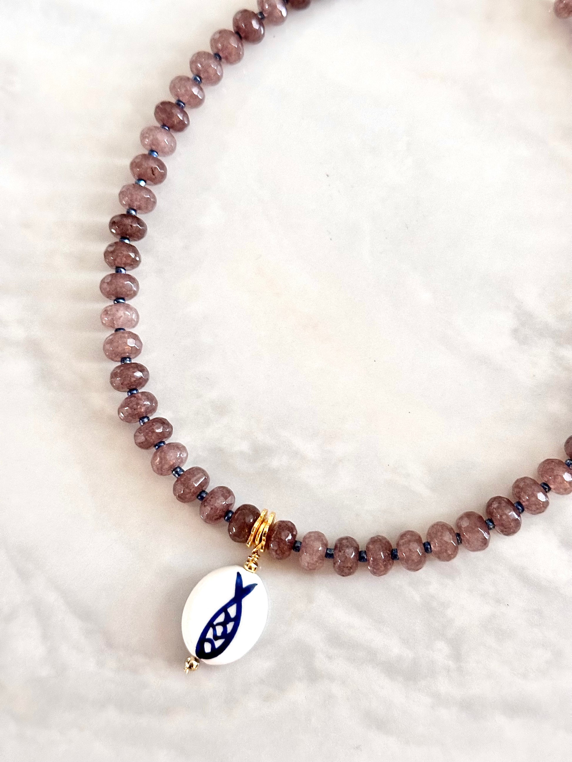 Beaded necklace with a fish charm on a white background
