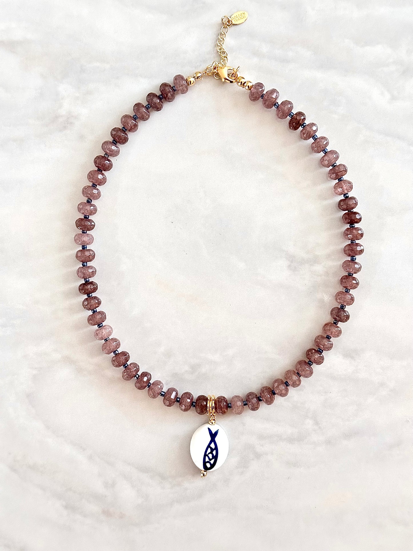 Necklace with purple beads and a fish charm on a white background