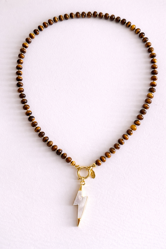 Necklace with Tiger Eye agate beads and a mother of pearl light bolt pendant on a ligh background