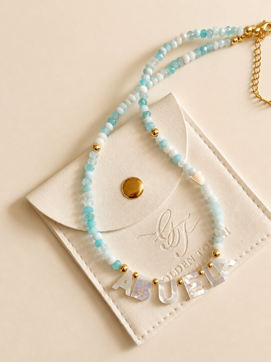 Necklace with 'ABUELA' beads on a beige card with a brand logo.