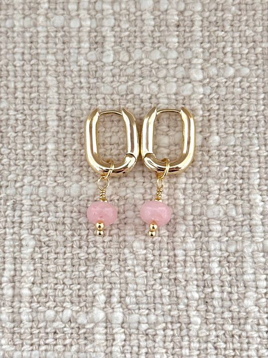 Gold hoop earrings with pink beads on a textured beige surface