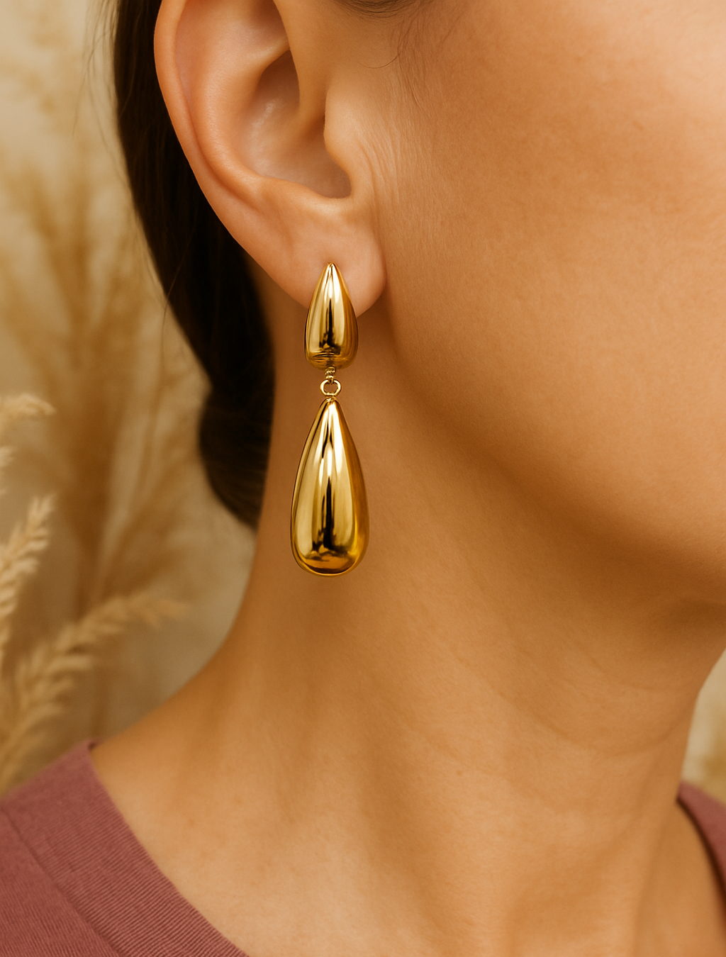 Gold teardrop earring worn by a person with a neutral background
