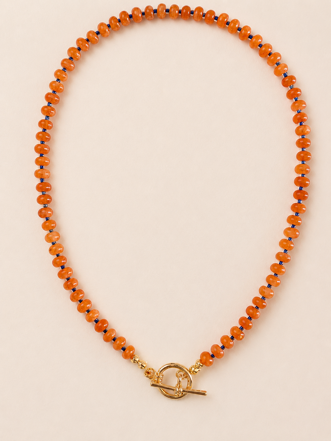 An orange beaded necklace with small natural beads and a gold toggle clasp, displayed on a light beige background.