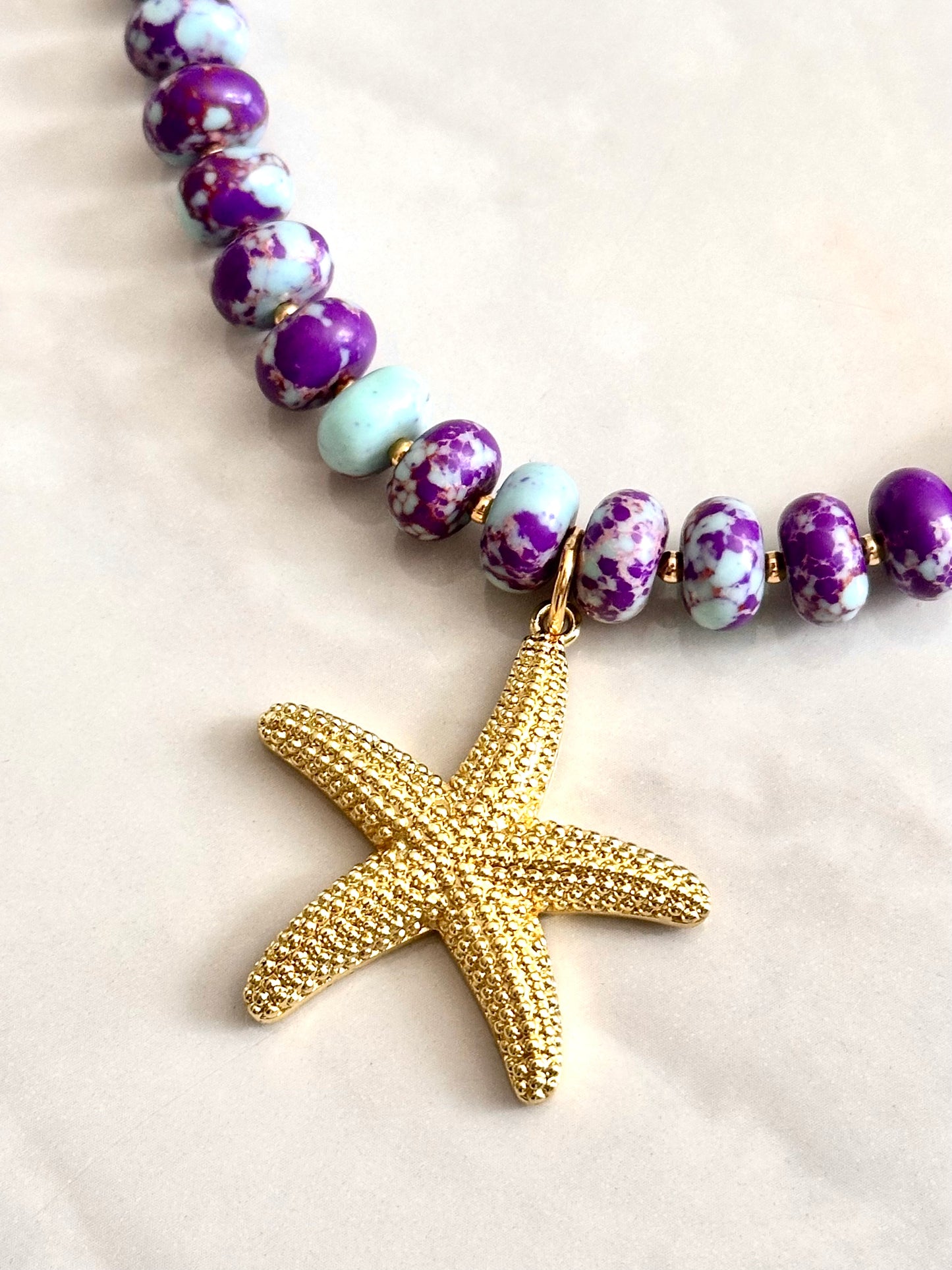 Necklace with purple and white beads and a gold starfish pendant on a light background