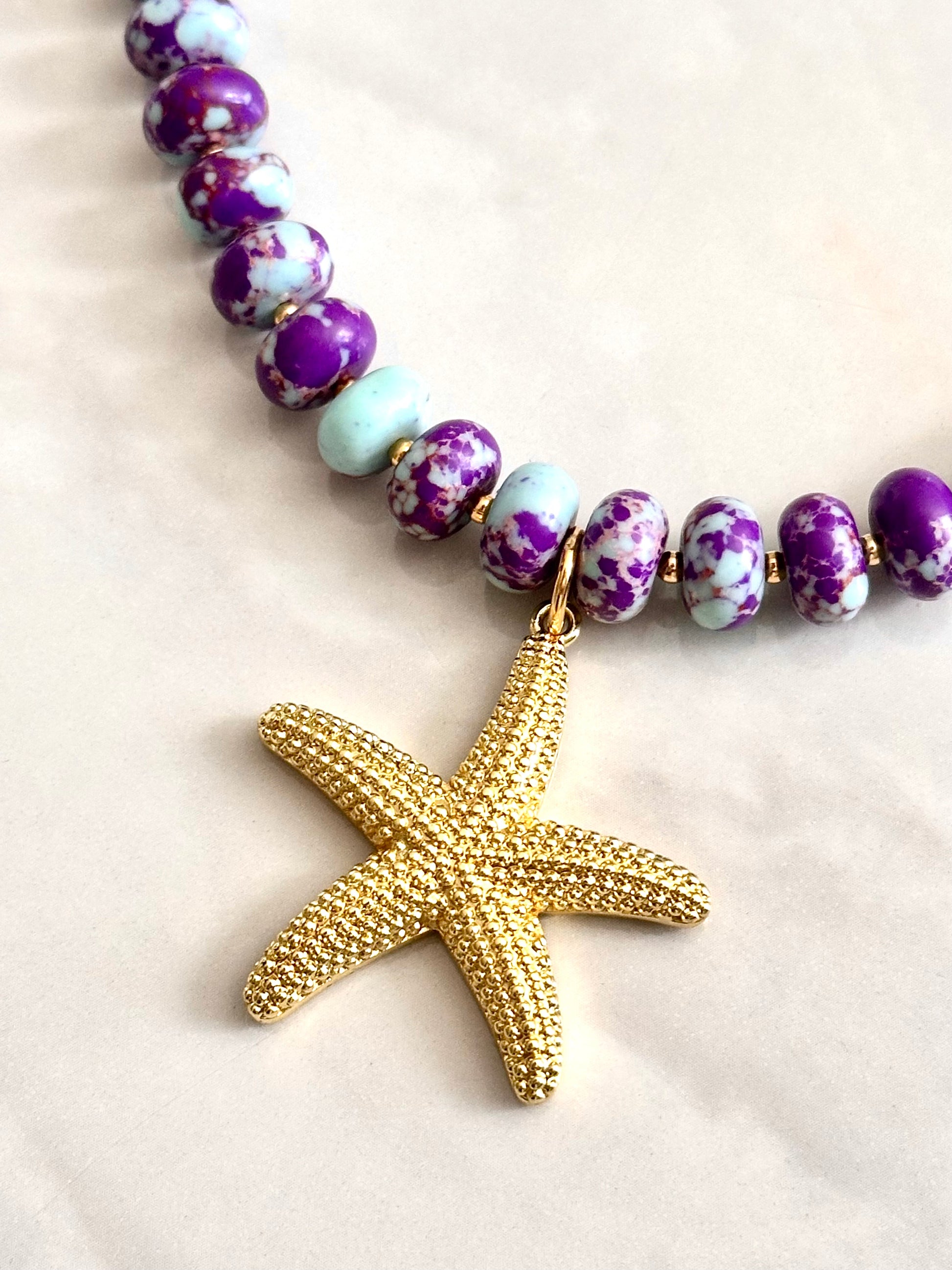 Necklace with purple and white beads and a gold starfish pendant on a light background
