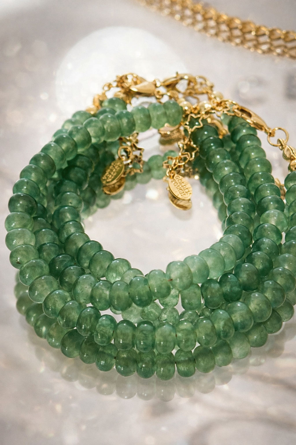 Green beaded bracelets with gold chains on a reflective surface