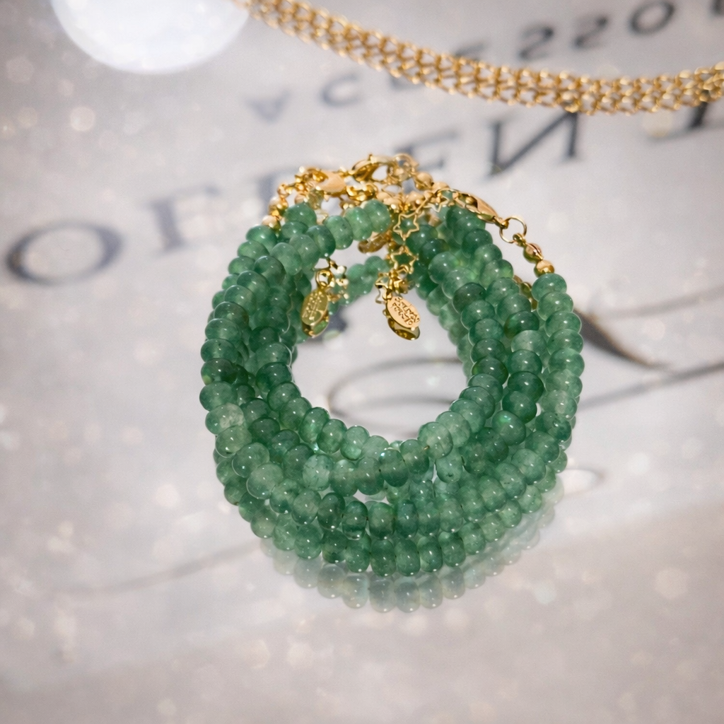 Green beaded bracelet with gold chain on a textured surface