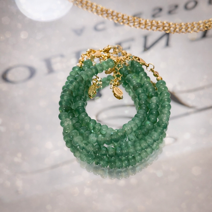 Green beaded bracelet with gold chain on a textured surface