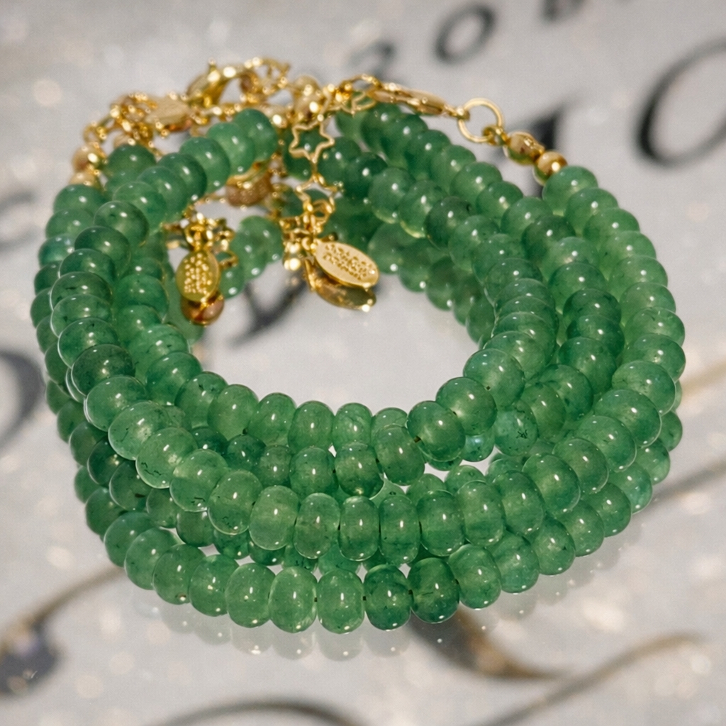 Stack of green beaded bracelets with gold accents on a blurred background