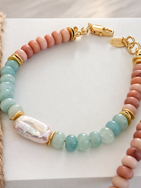 Beaded bracelet with peach, turquouse, and gold accents and a flat pearl on a white background. coastal bracelet.