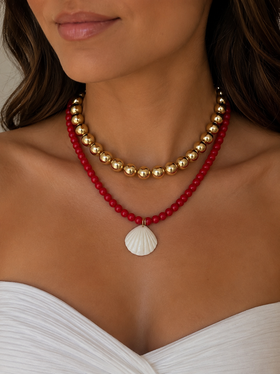 Close-up of a woman wearing a red and gold beaded necklace with a shell pendant.