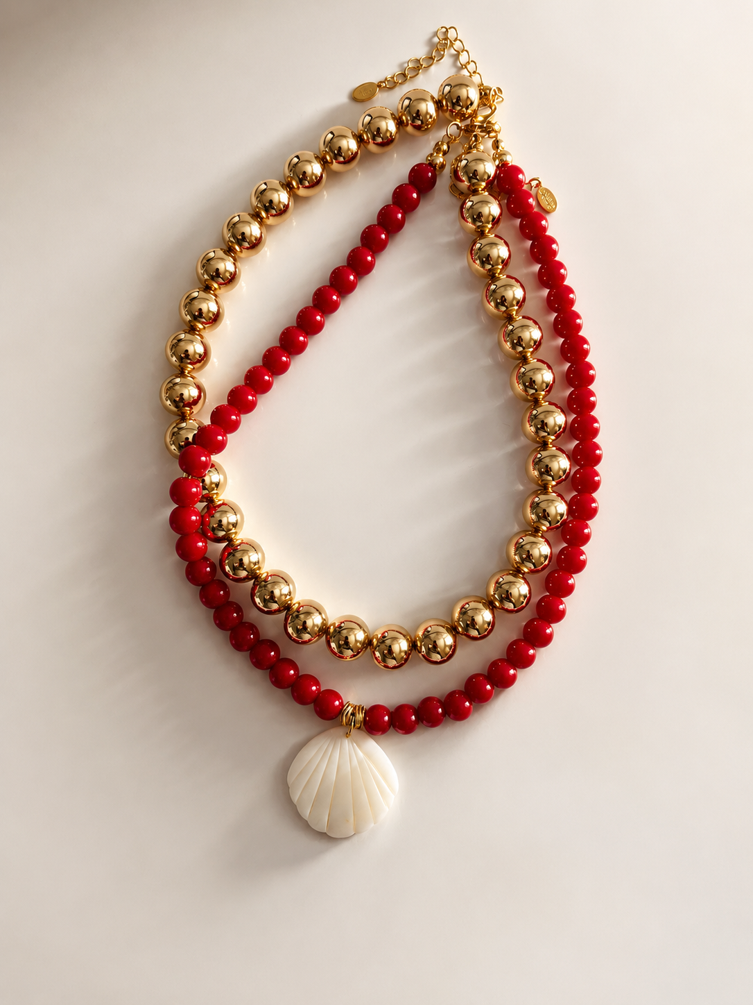 Double-layered necklace with red beads and a shell pendant on a light background