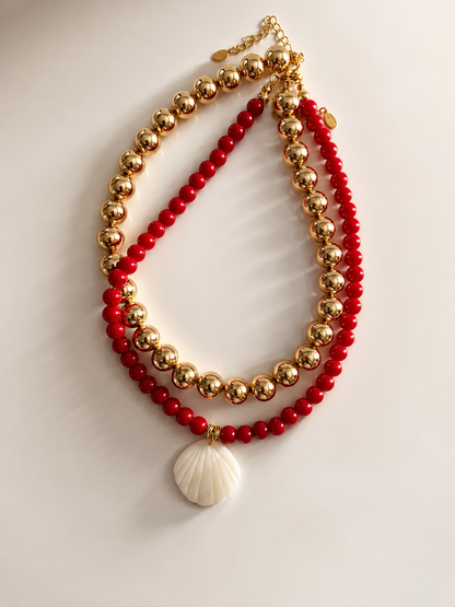 Double-layered necklace with red beads and a shell pendant on a light background