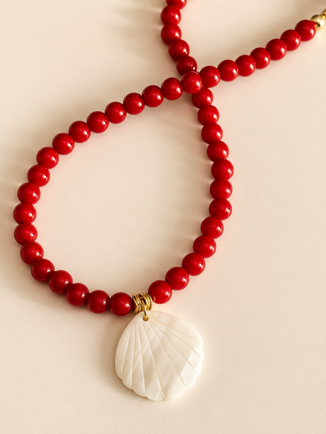 Red beaded necklace with a white shell pendant on a beige background