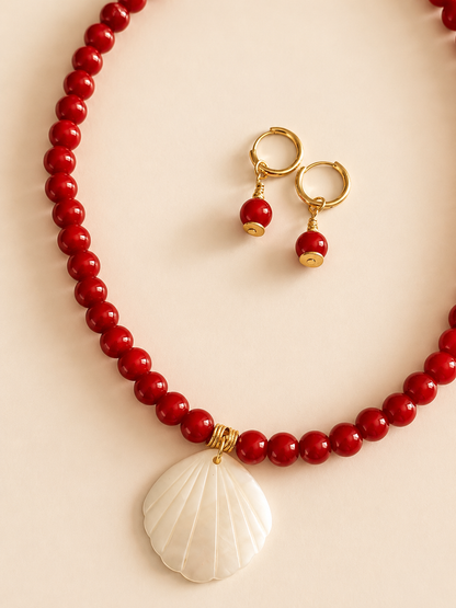 Red beaded necklace with a shell pendant and matching earrings on a beige background