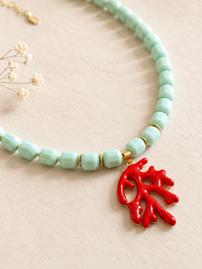 Necklace with turquoise beads and a red coral-like pendant on a beige background
