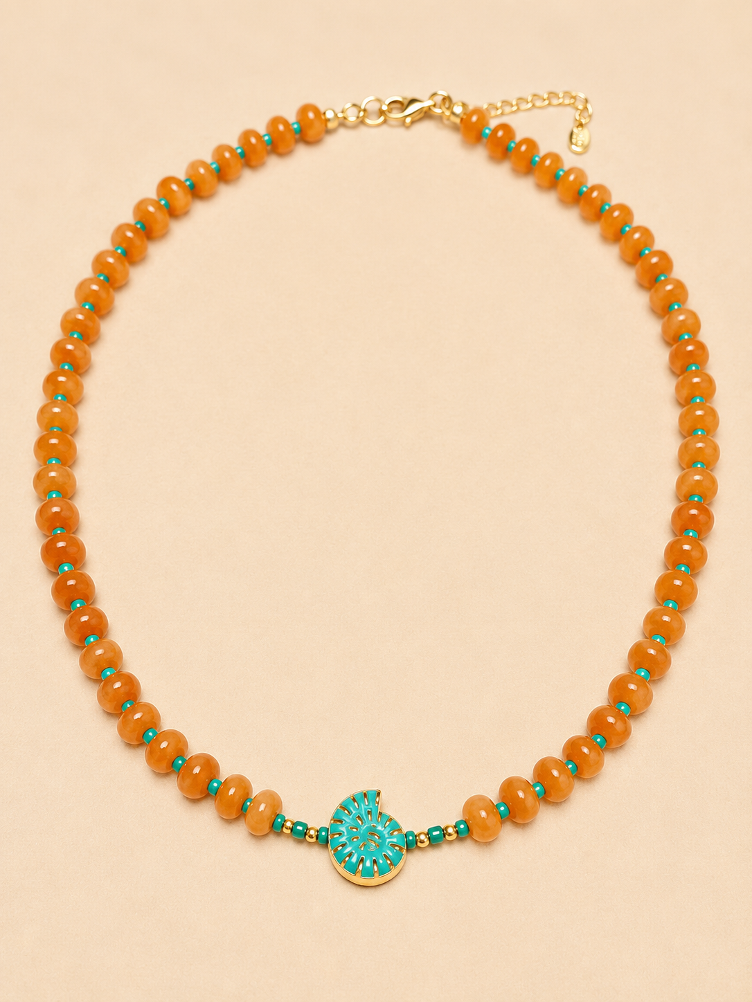 A beaded necklace featuring round orange agate beads accented with small turquoise blue beads, a central turquoise shell shaped charm with gold detailing, and a gold clasp on a light beige background.