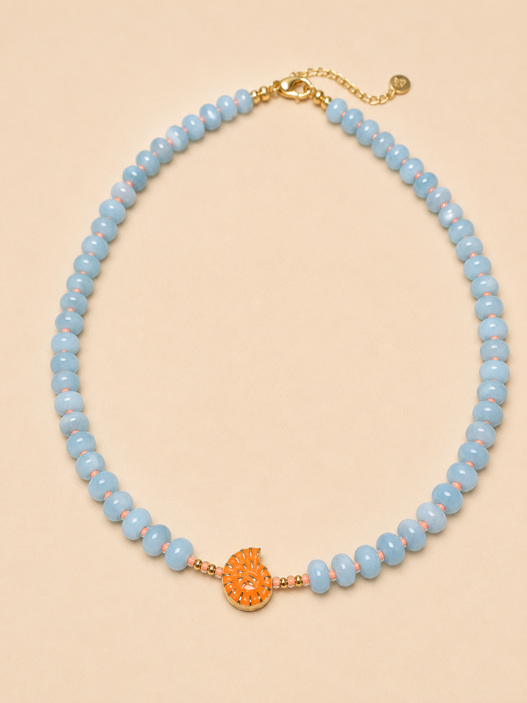 A light dusty blue faceted agate bead necklace with a central textured neon orange  shell charm and gold-tone hardware, displayed on a solid beige background.