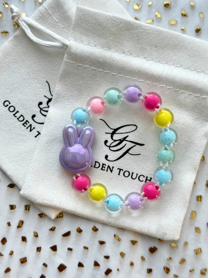Colorful beaded bracelet with a bunny charm on a Golden Touch branded drawstring bag.