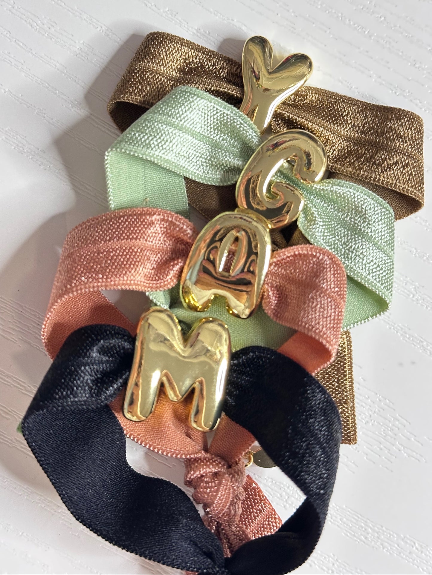 Set of colorful scrunchies with gold letter charms on a light background